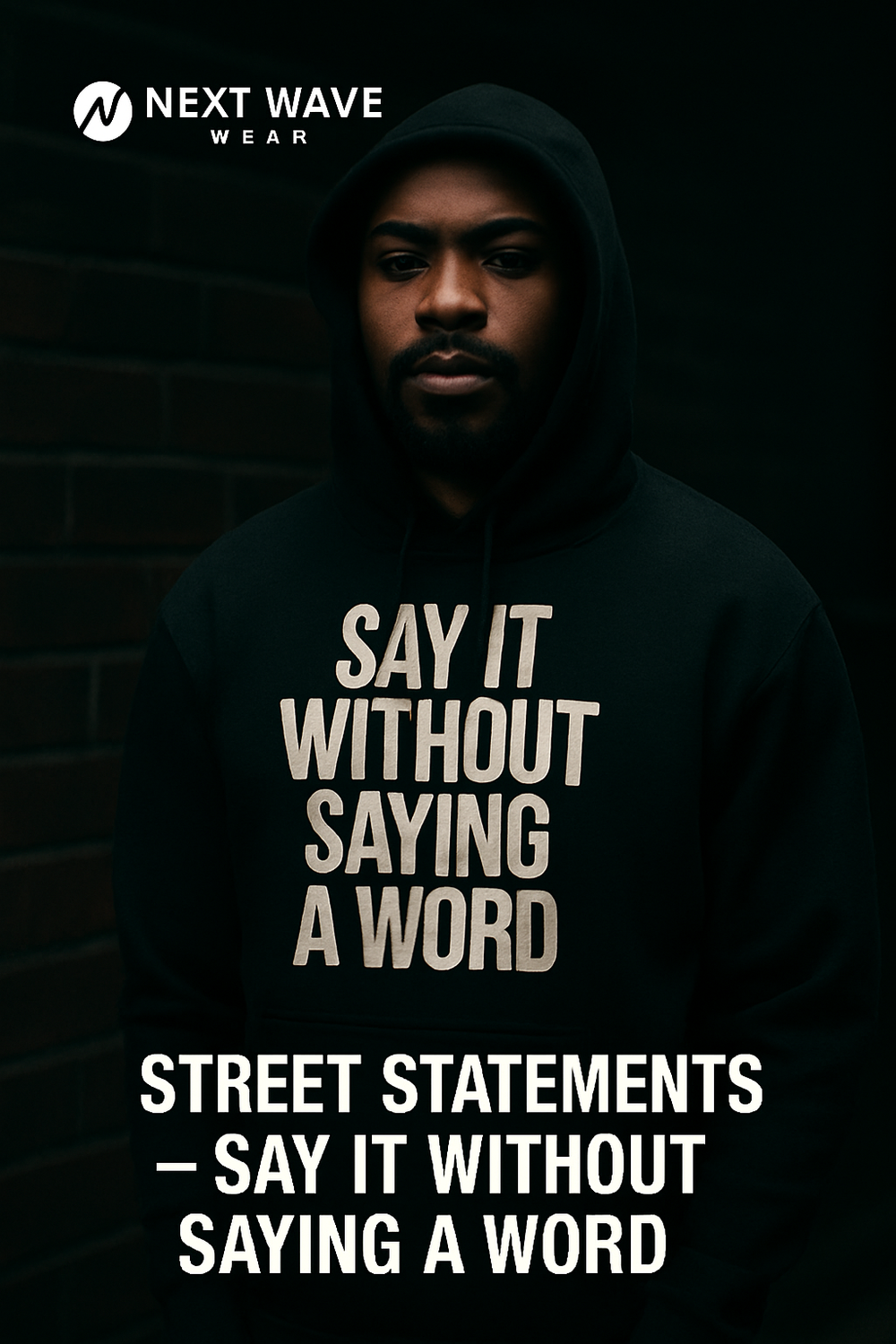 Model in hoodie with bold “Say It Without Saying A Word” graphic, standing against brick wall. Urban, moody streetwear from the Street Statements collection by Next Wave Wear.